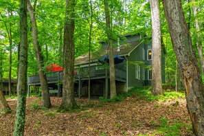 Une cabane entourée de grands arbres, avec une terrasse et un parasol rouge.