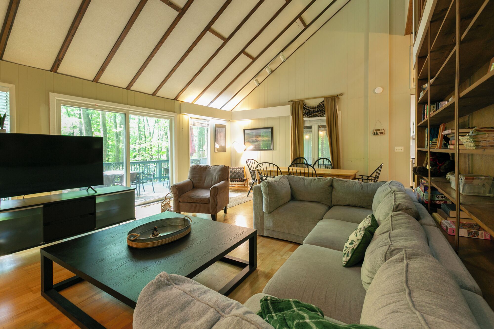 A living room with a sectional sofa, a coffee table, a TV, and a dining area with chairs and a table.