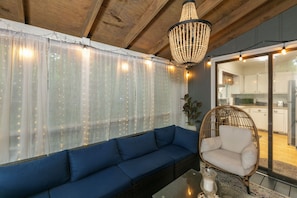 A cozy room with a blue sofa, a wicker chair, a glass coffee table, and a chandelier.