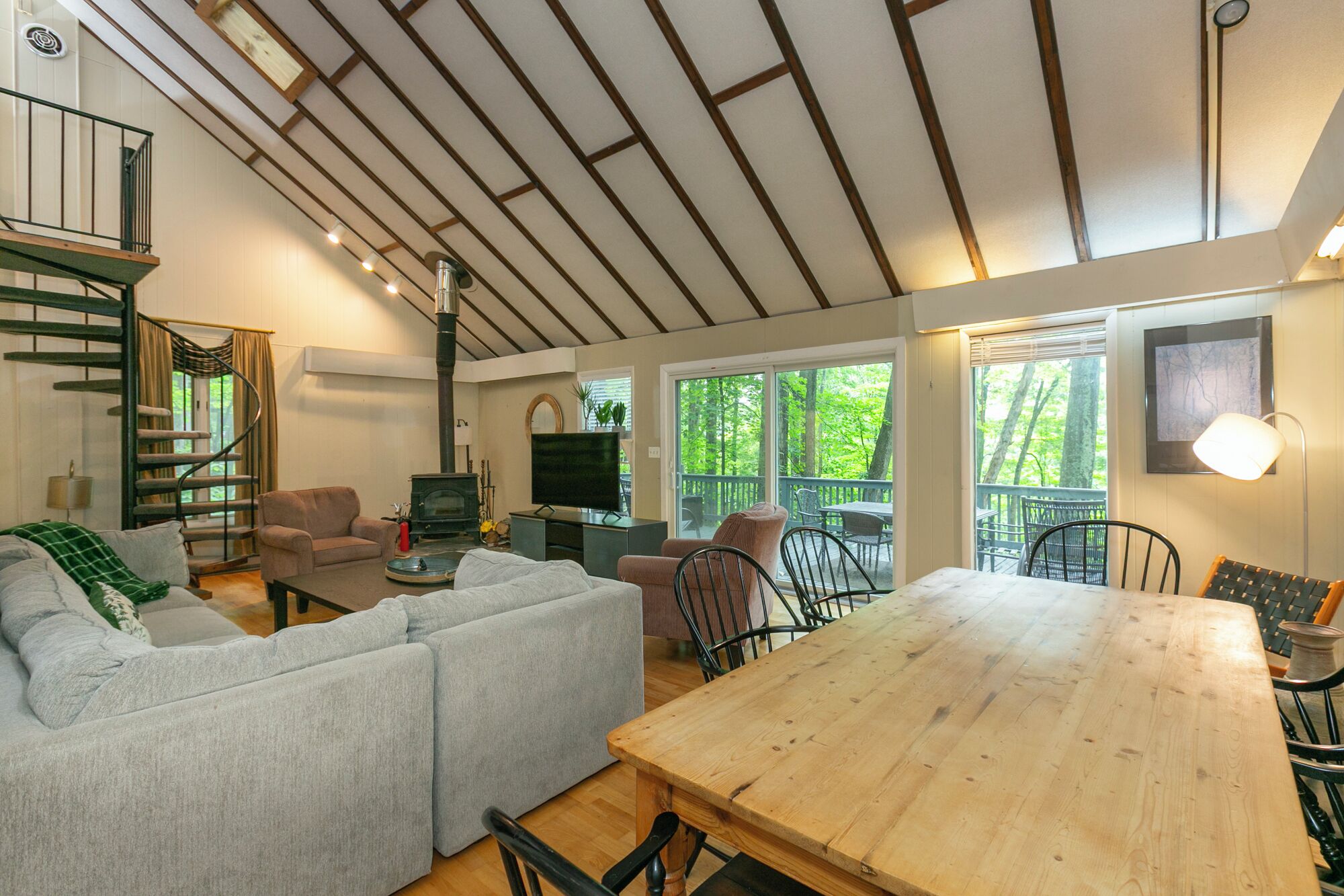 A cozy living room with a sofa, a wooden dining table, a fireplace, and a staircase.