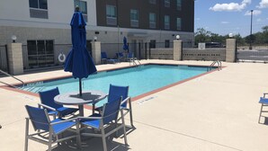 A swimming pool with lounge chairs and umbrellas, a building with multiple windows, and a fenced area. - Holiday Inn Express & Suites Junction by IHG (Junction)
