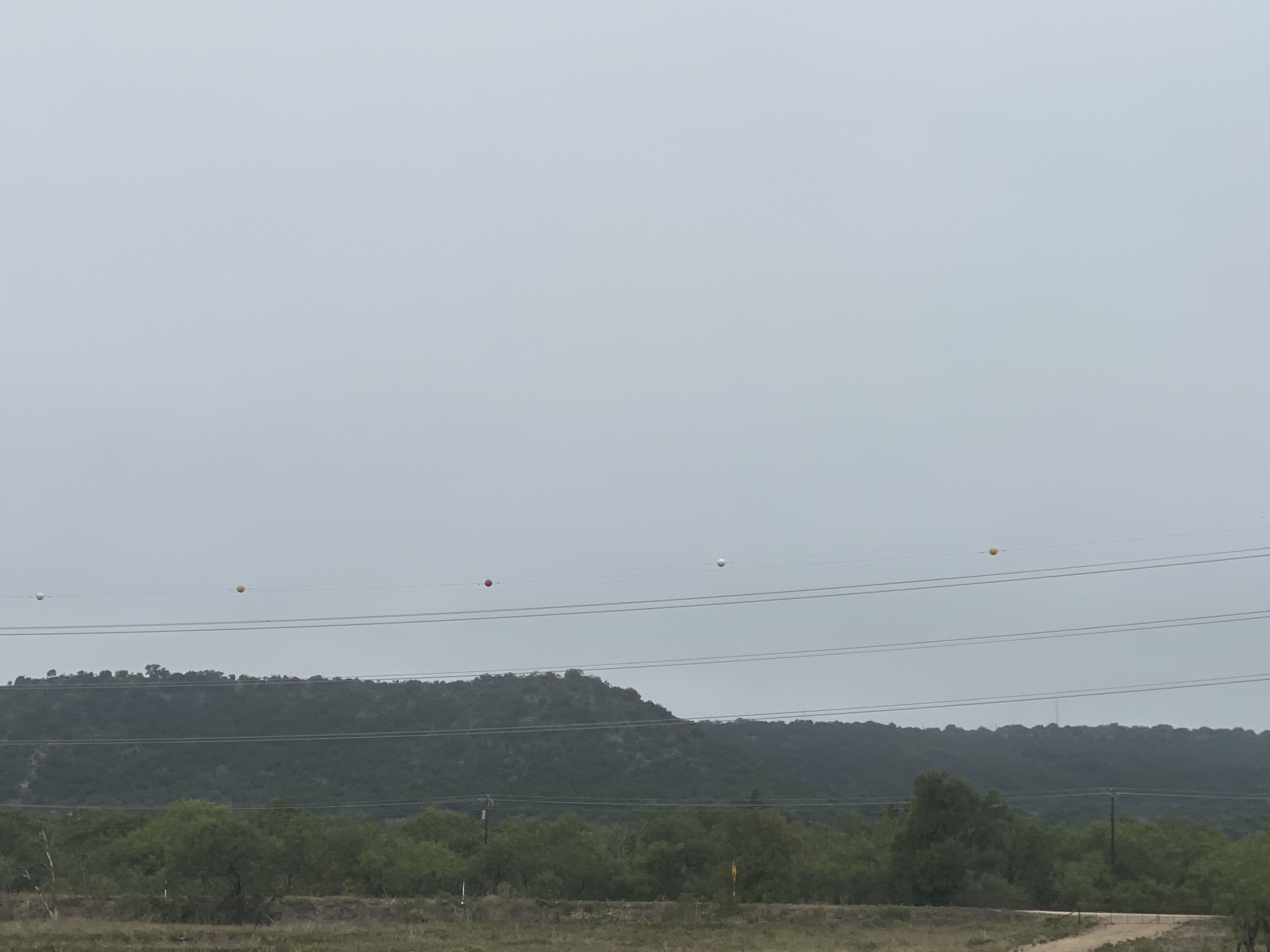 Paisaje rural con un sendero de tierra, líneas eléctricas y una colina con vegetación densa.