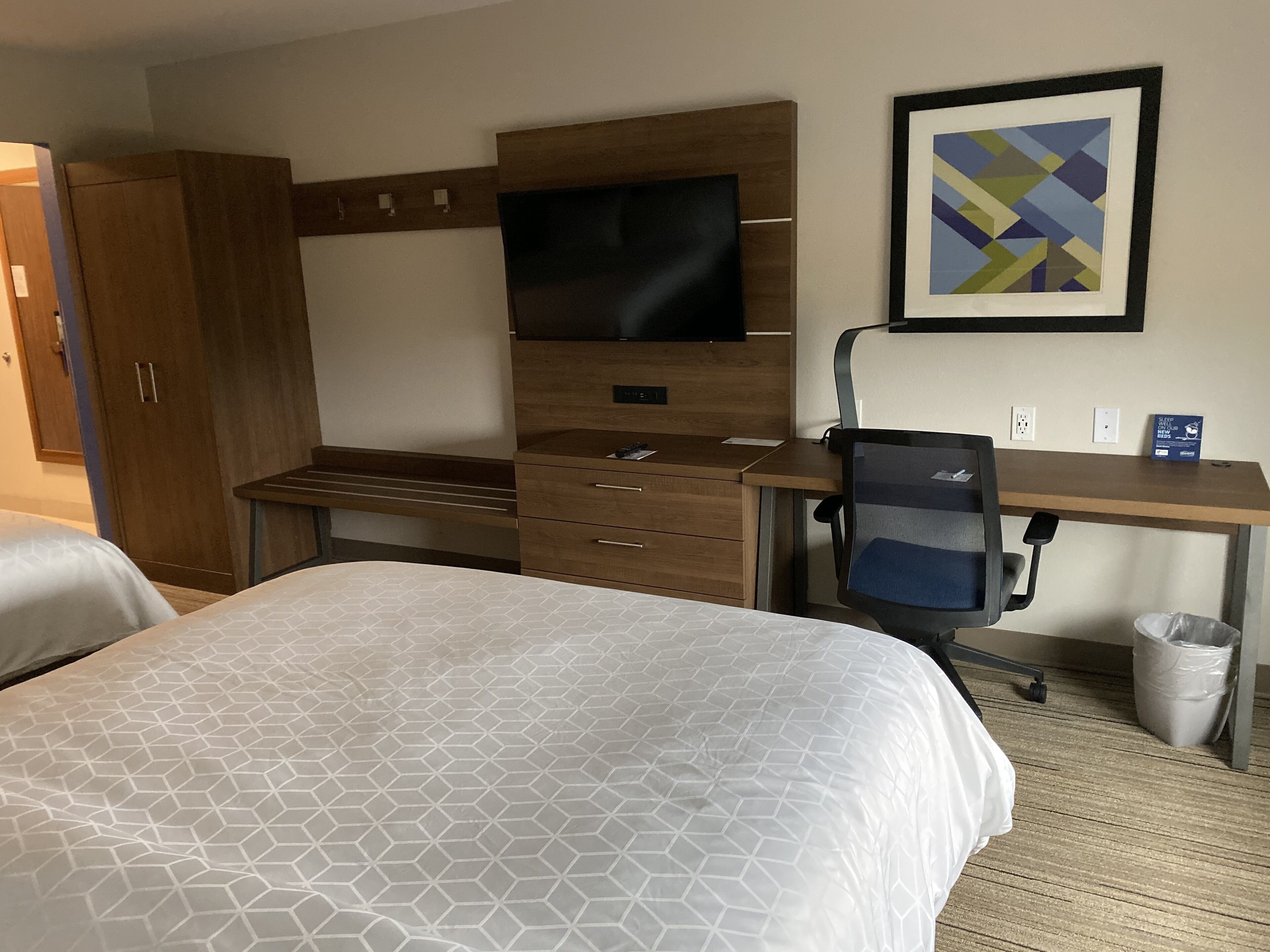 Een hotelkamer met twee bedden, een bureau, een stoel, een televisie en een kunstwerk in een lijst aan de muur.