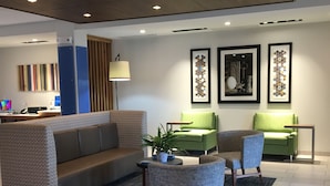 A modern lobby with a sofa, two green armchairs, a small table with a plant, and framed artwork on the wall. - Holiday Inn Express & Suites Junction by IHG (Junction)