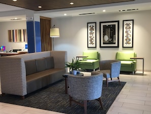 A modern lobby with a sofa, two green armchairs, a small table with a plant, and framed artwork on the wall. - Holiday Inn Express & Suites Junction by IHG (Junction)