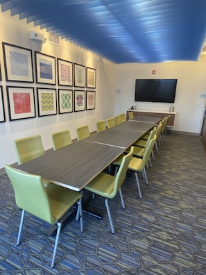 A conference room with a long table and chairs, a flat-screen TV, and framed artwork on the wall.