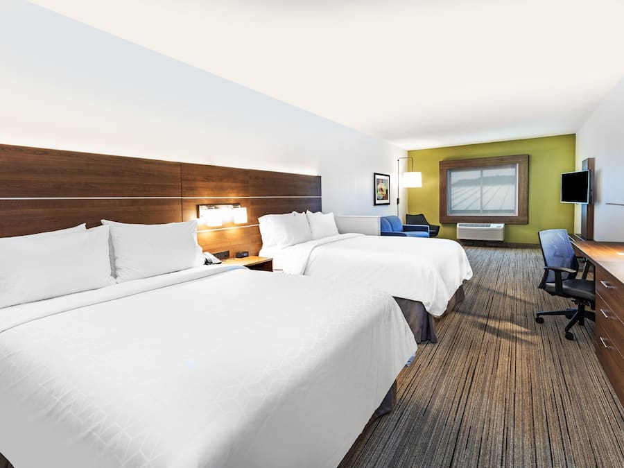 Quarto de hotel com duas camas, uma escrivaninha, uma cadeira, uma televisão e janela com vista.