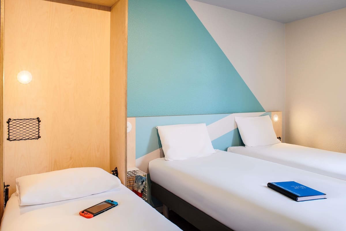 Une chambre d’hôtel avec deux lits, une porte en bois, un mur bleu clair et un plafond blanc.