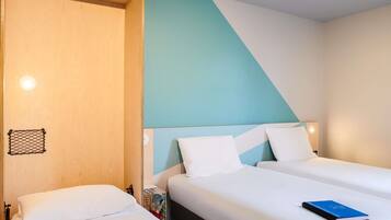 Ein Hotelzimmer mit zwei Betten, einer Holztür, einer hellblauen Wand und einer weißen Decke.