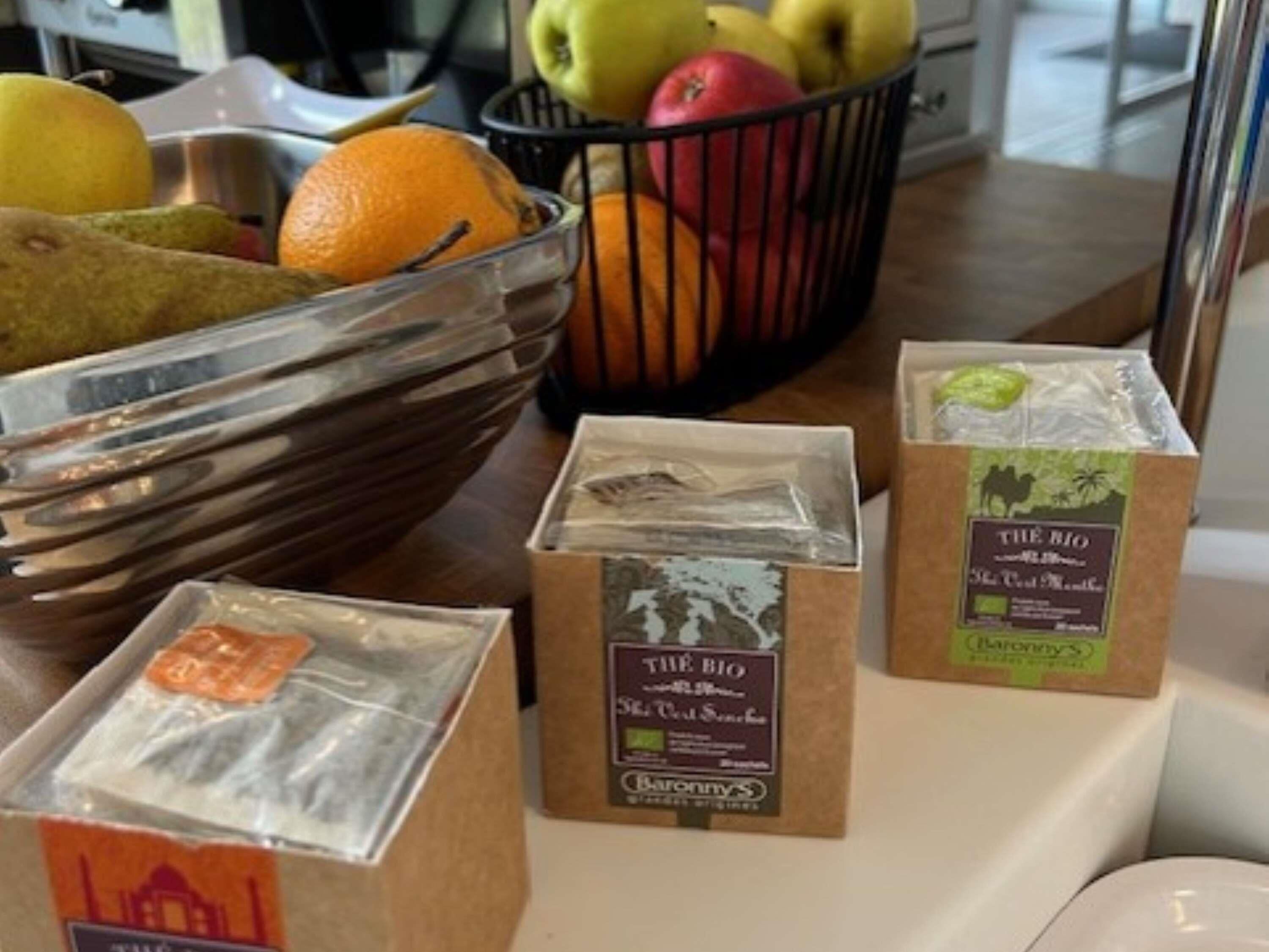 A kitchen counter with a fruit basket containing apples, oranges, and pears, and three packaged food items labeled 'THE BIO.'