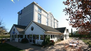 A hotel with a large building and a smaller annex with a covered patio area. - Hôtel Ibis Budget Nantes Ouest Atlantis Couëron (Coueron)