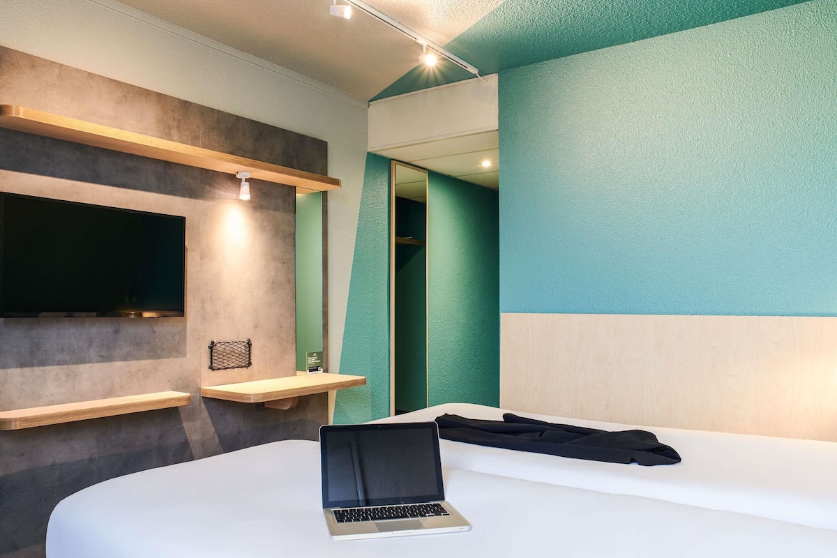 Une chambre d’hôtel moderne équipée d’un lit, d’un ordinateur portable, d’une télévision et d’un miroir.