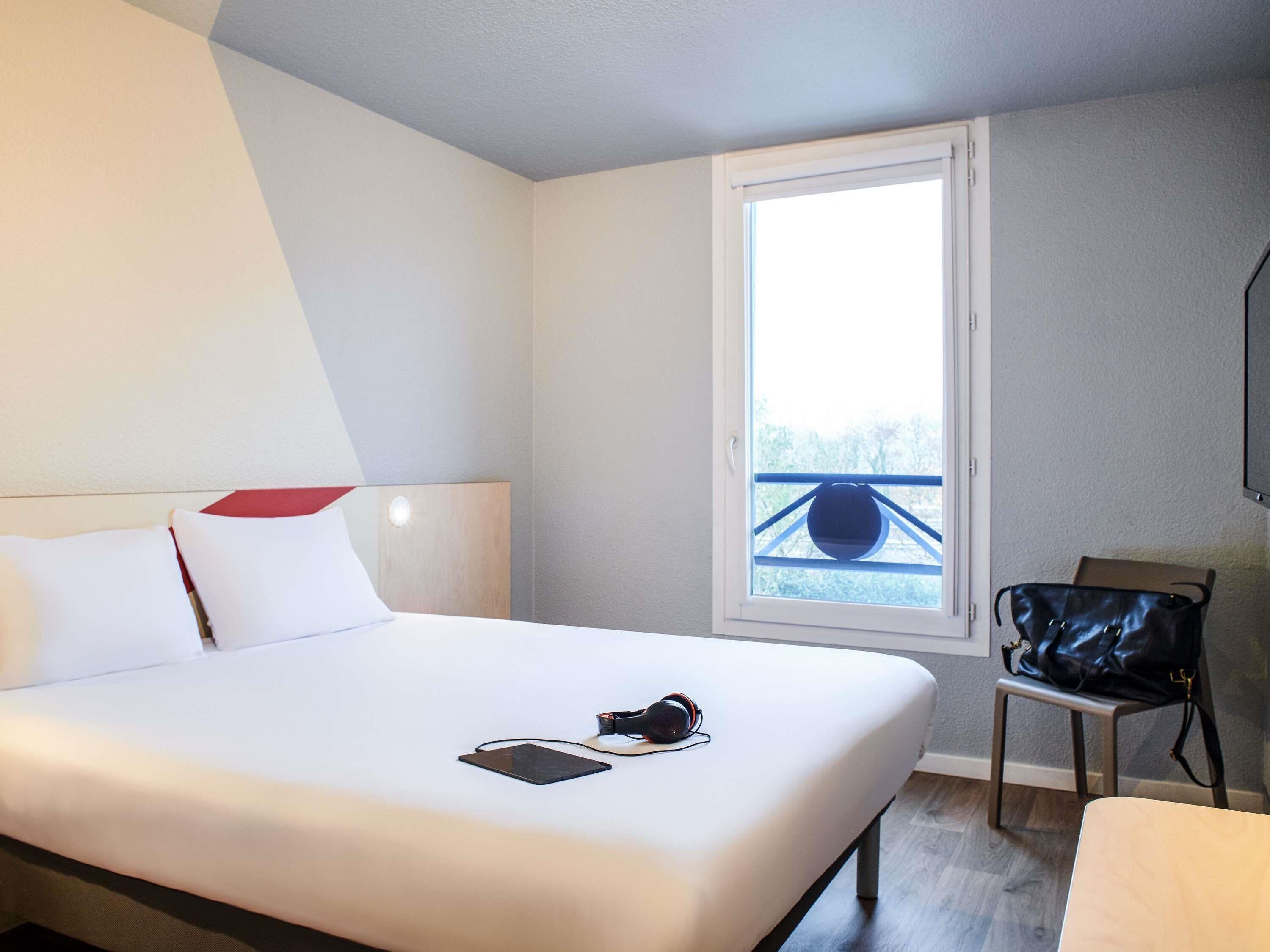 A hotel room with a bed, a window with a view, a chair, and a TV.