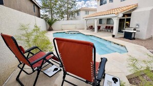 Ein Schwimmbad mit Liegestühlen, einer Grillgelegenheit und einer überdachten Terrasse.