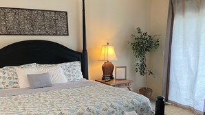 Una camera d'albergo ordinata con un letto, un comodino, una lampada e una pianta in vaso.