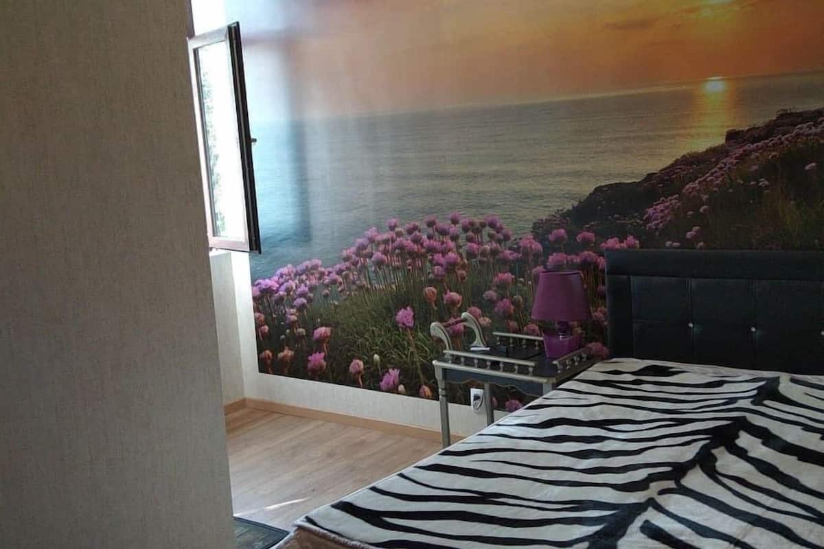 Ein Schlafzimmer mit einem Bett mit Zebra-Muster, Blick auf den Ozean durch ein großes Fenster und einem Sonnenuntergangsgemälde an der Wand.