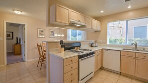 A kitchen with a central island, stove, oven, and dishwasher. There are wooden cabinets, a window with blinds, and a door leading to another room. - "The Fontana" 4bedrooms,  Hot Tub, Patio Mister,Pets Welcome, 5G Fiber Internet! (Albuquerque)