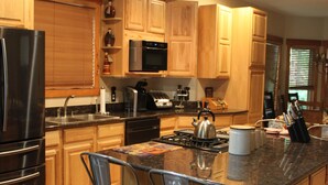 Una cocina moderna con armarios de madera, un refrigerador de acero inoxidable, un microondas y una estufa a gas. Hay dos taburetes de bar y una isla grande con un hervidor.