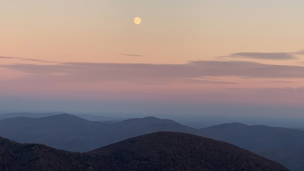 Un paisaje montañoso con una luna visible en el cielo.