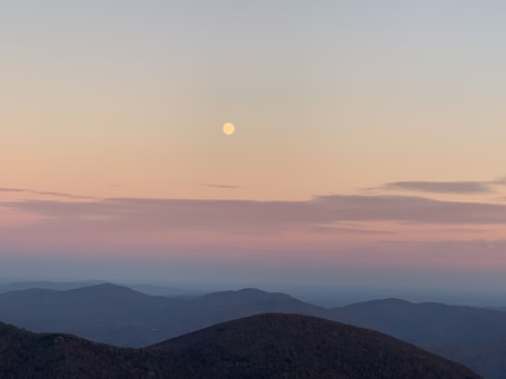 A mountain landscape with a visible moon in the sky.