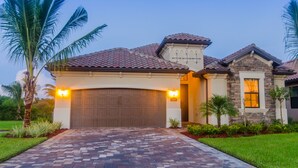 A residential house with a garage, a stone exterior, and a brick driveway.