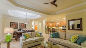 A spacious living room with a sofa set, a glass coffee table, and a dining area with wooden chairs and a chandelier.