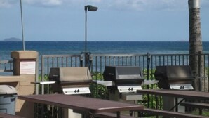 An outdoor seating area with grills and a flag, overlooking the ocean. - Maalaea 5 star Island Sands 100 2 bed Oceanfront (Wailuku)
