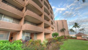 A multi-story hotel with balconies, a well-maintained garden, and palm trees. - Maalaea 5 star Island Sands 100 2 bed Oceanfront (Wailuku)