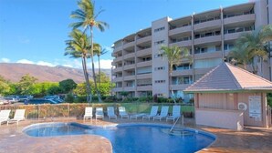 A hotel with a swimming pool, palm trees, and a mountainous backdrop. - Maalaea 5 star Island Sands 100 2 bed Oceanfront (Wailuku)