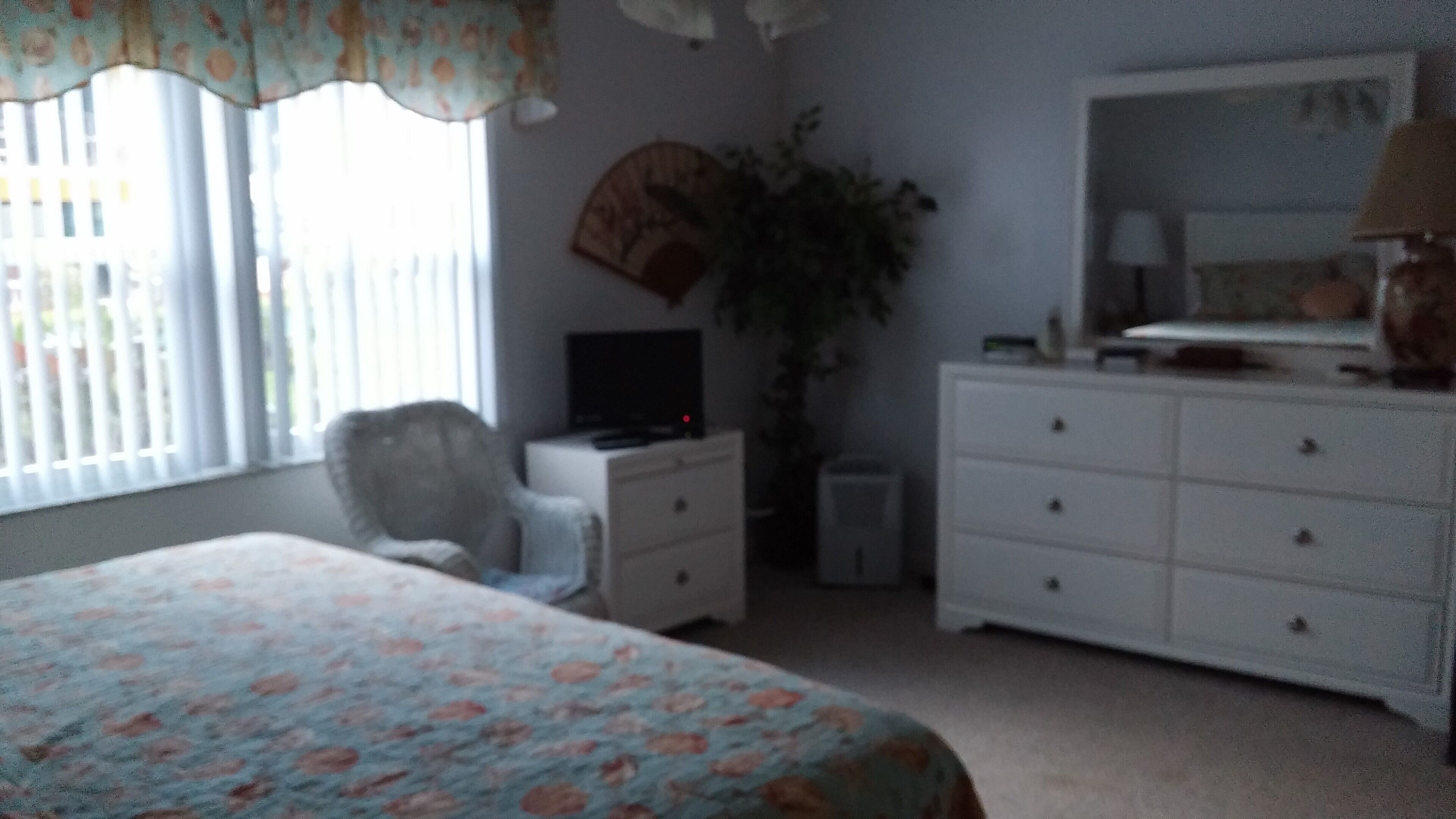 A bedroom with a bed, a dresser, a chair, a television, and a large window.