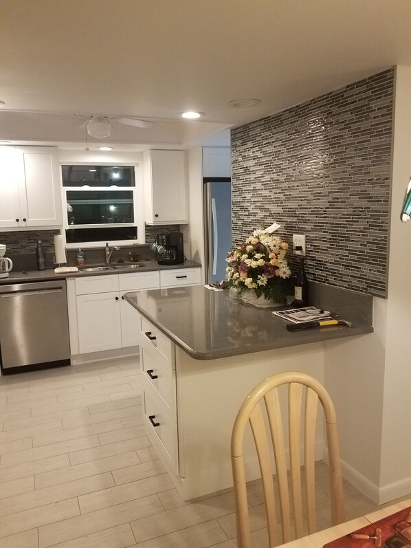 A modern kitchen with white cabinets, a stainless steel dishwasher, a coffee maker, and a decorative vase with flowers.