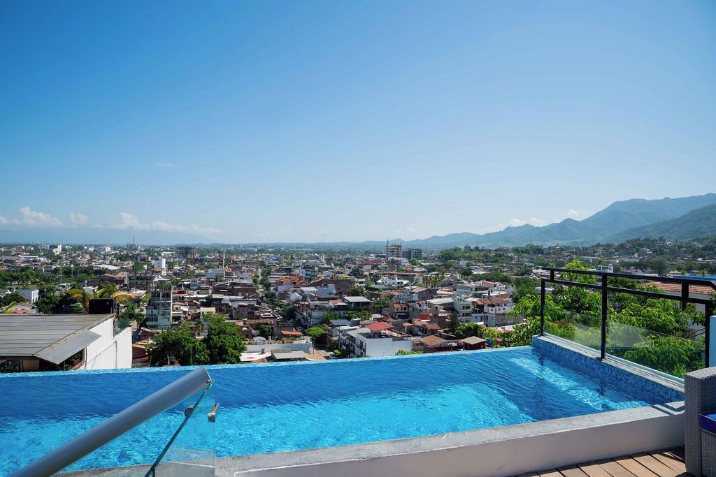 A rooftop infinity pool with a city view, surrounded by buildings and mountains.