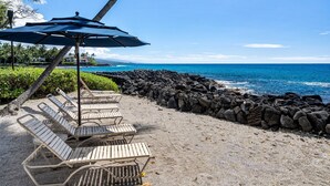 Eine Strandbucht mit Liegestühlen und Sonnenschirmen, einer felsigen Küstenlinie und Blick auf den Ozean.
