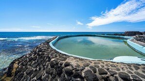 Ein Steinpool mit blauem Himmel und Blick auf den Ozean im Hintergrund.