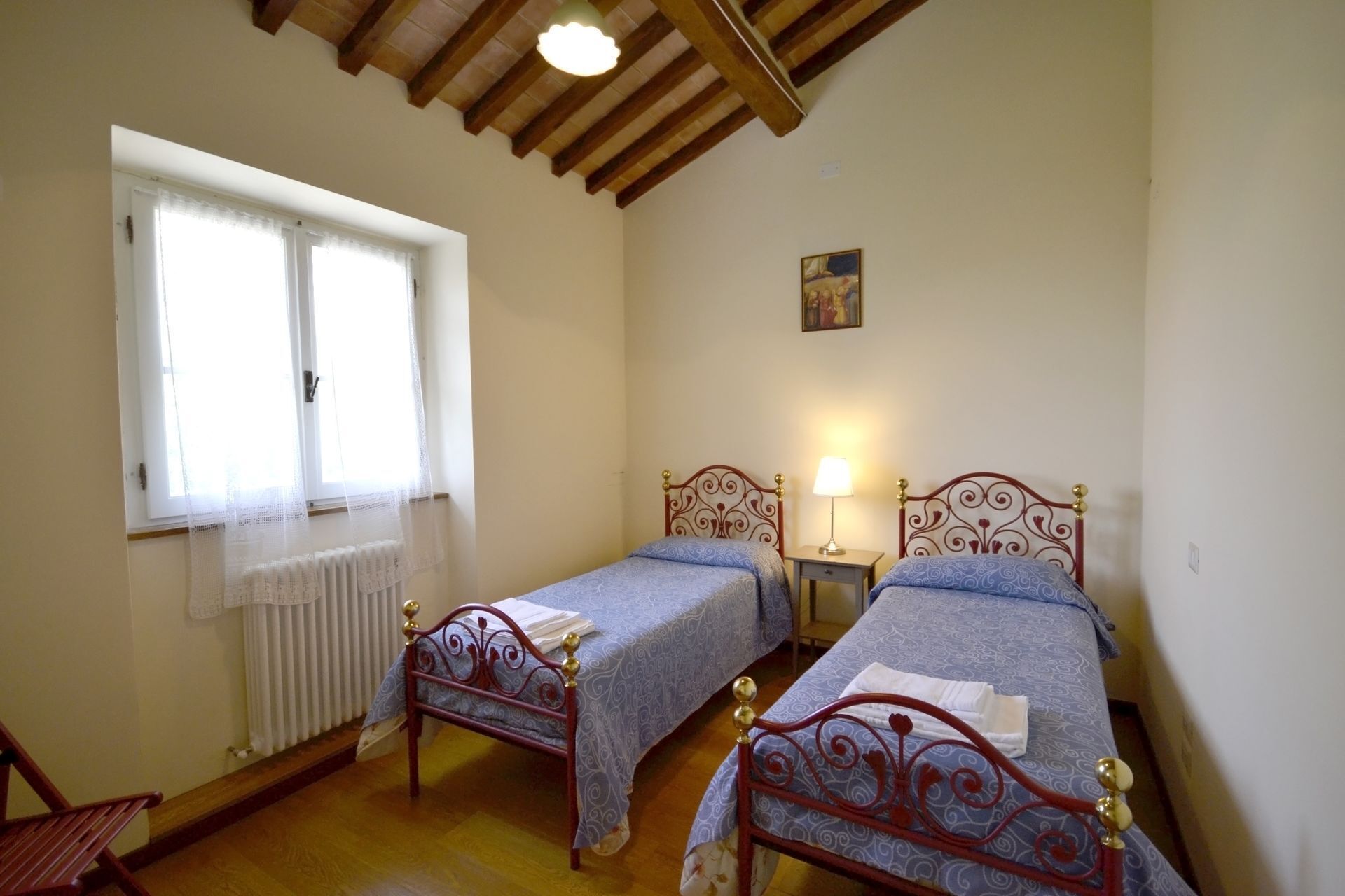A room with two beds, a radiator, a window with sheer curtains, and a painting on the wall.