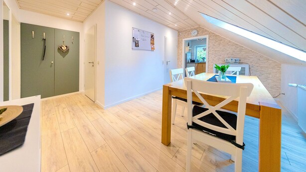 A modern kitchen with a skylight, a dining area with a wooden table and white chairs, and a green door.