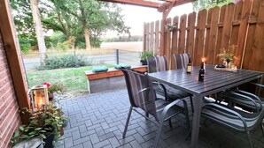 An outdoor patio with a brick floor, a wooden fence, and a table with chairs.