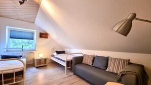 A compact, well-lit room with a bunk bed, a sofa, a small table, and a window with blinds.
