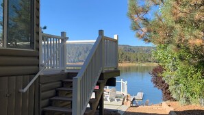 Una cabaña con terraza que da a un lago, con escalera y zona de estar al aire libre.