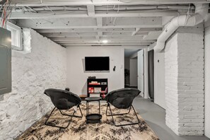 A room with a white brick wall, a flat-screen TV mounted above a bookshelf, and a patterned rug on the floor.
