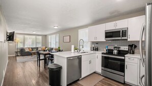 Una cocina moderna con armarios blancos, electrodomésticos de acero inoxidable y una zona de comedor con sofá y mesa.