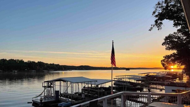 A waterfront dock with a flag, boats, and a sunset view.