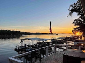A waterfront dock with a flag, boats, and a sunset view. - Powell Lakehouse | Hot Tub, Dock & Sunset Views | Featured on Staycation episode (Sunrise Beach)