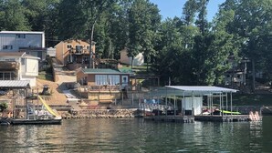 A waterfront property with a dock, a covered boat launch, and a house with a deck and stairs leading to a second floor.