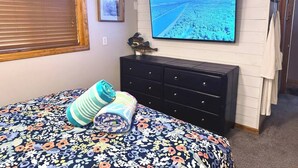A bedroom with a bed, a dresser, a television on the wall, and a window with blinds.