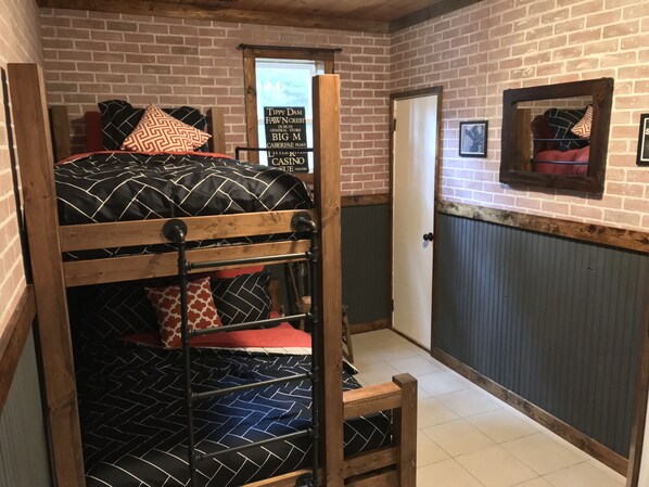 A bunk bed with patterned bedding, a door with a sign, and a framed picture on the wall. - The Industrial Suite 2 Bed 1 Bath Cabin Near Trails and Big Manistee River! (Wellston)