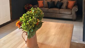 Un soggiorno con soffitto in legno, un divano in pelle marrone, un orologio tondo a parete e una pianta in vaso su un tavolo di legno.