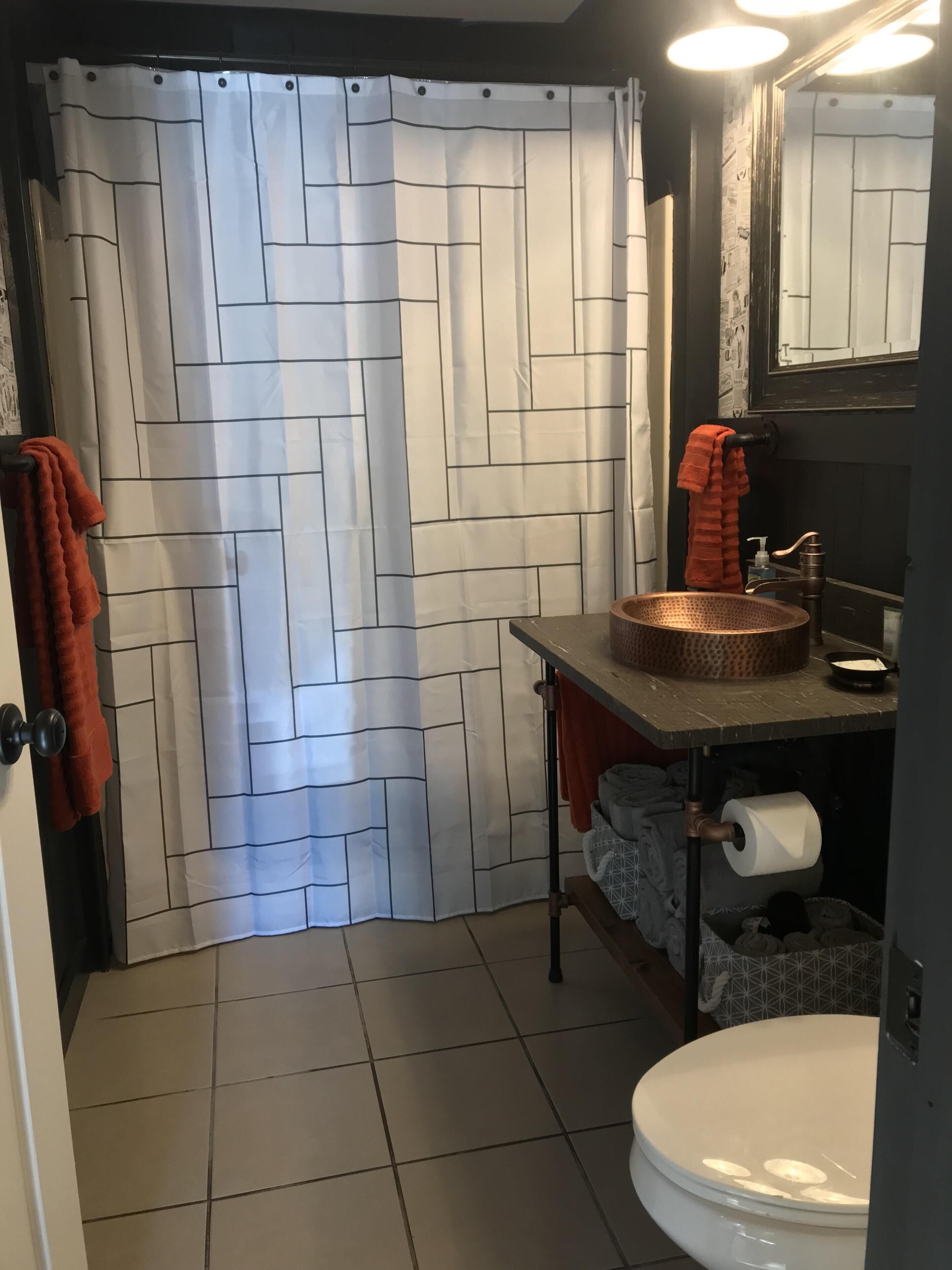Un baño con cortina de ducha estampada, un lavabo con recipiente de cobre, un inodoro y un espejo sobre el lavabo.