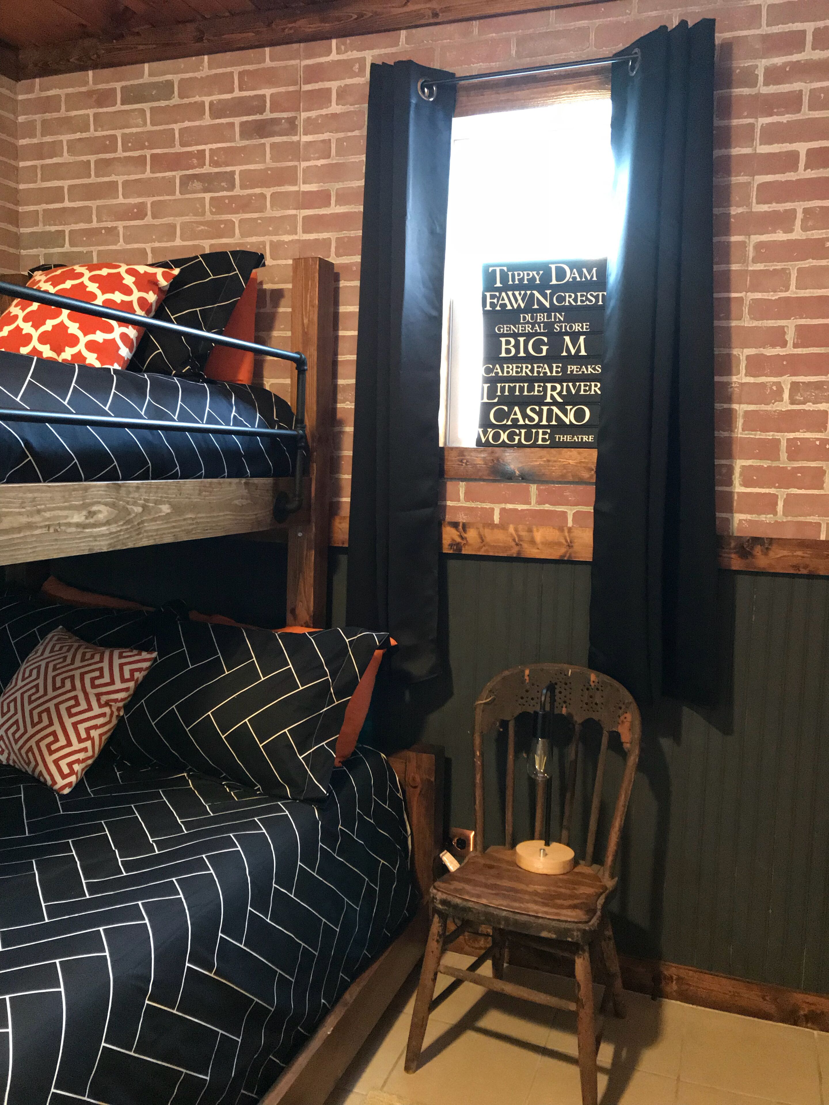 Una stanza con un letto a castello, una sedia di legno e una finestra con tenda.