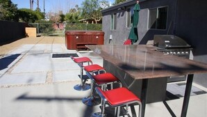 Une terrasse dotée d’un coin bar comprenant quatre tabourets rouges et un barbecue.